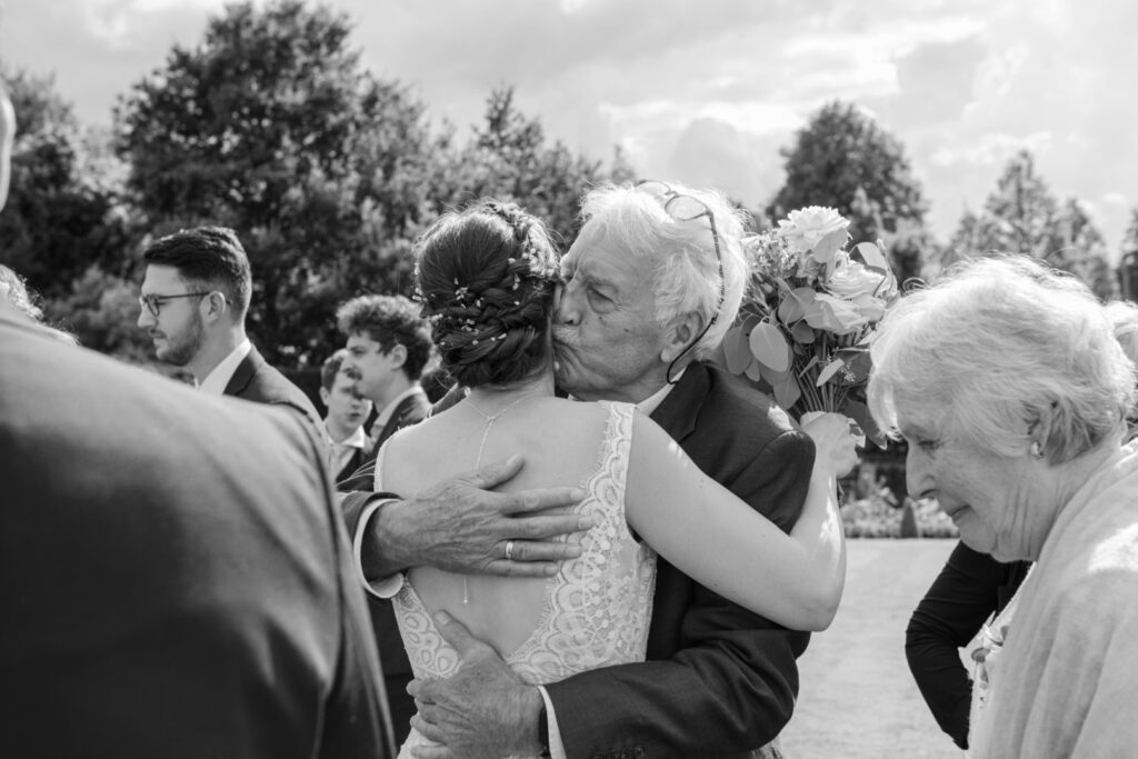A joyful embrace between a bride and her grandfather, surrounded by family members, capturing a heartfelt moment at the wedding celebration.