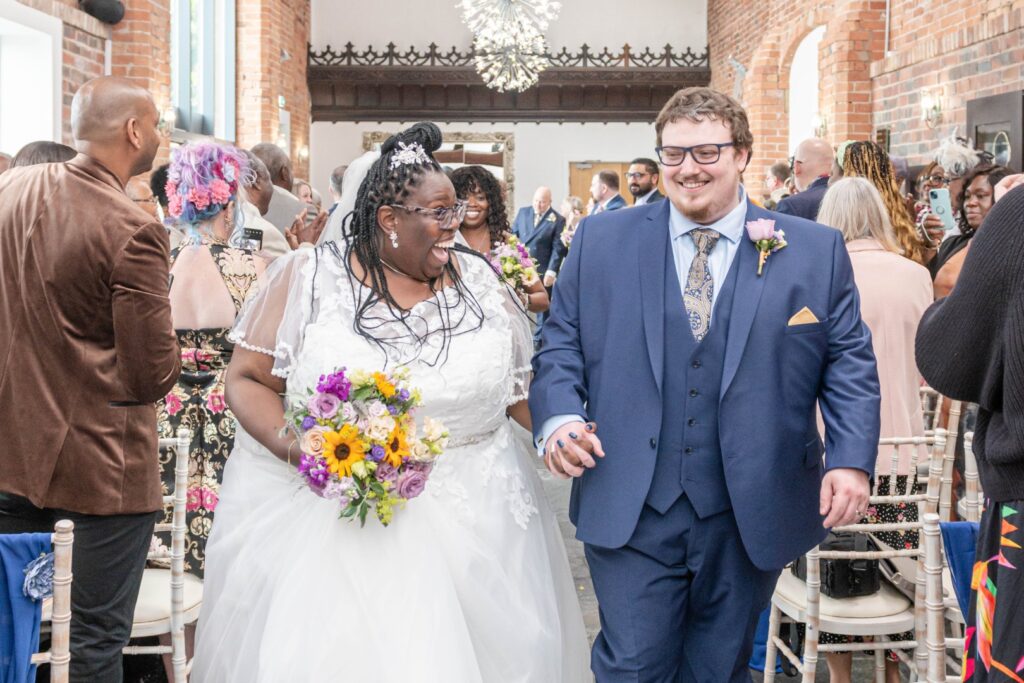Bride and groom laughing as they walk down the aisle – joyful wedding moment captured naturally by LB Photography