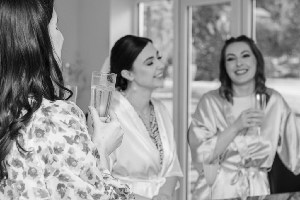 Bride and bridesmaids laughing while getting ready with champagne – candid morning wedding moment captured by LB Photography