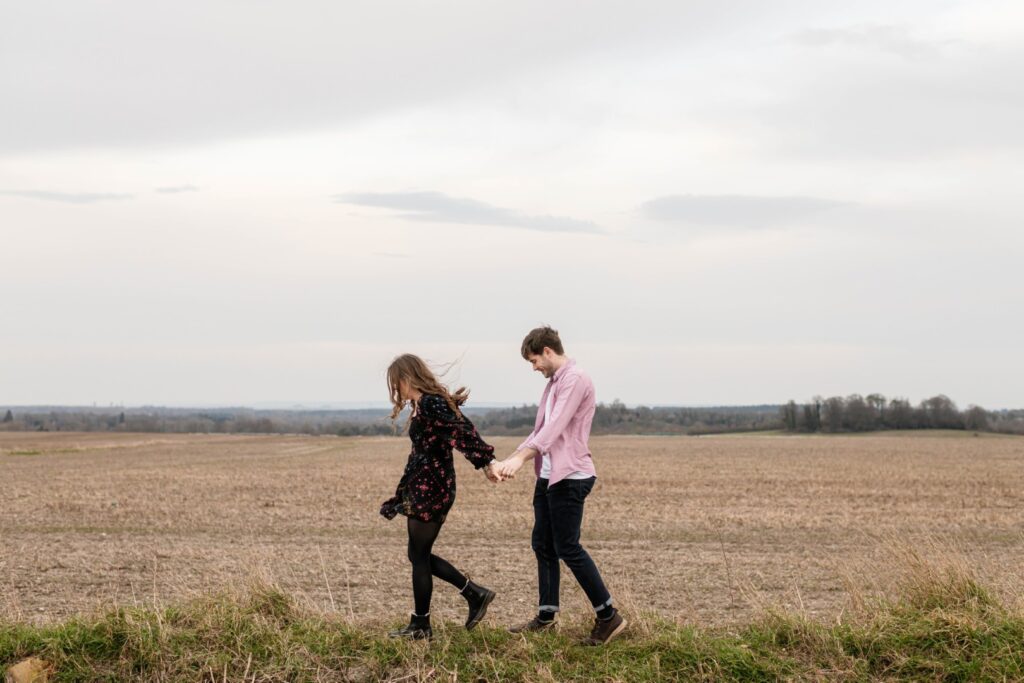 Engaged couple walking hand in hand through an open field at sunset, laughing together during a relaxed and natural pre-wedding shoot.