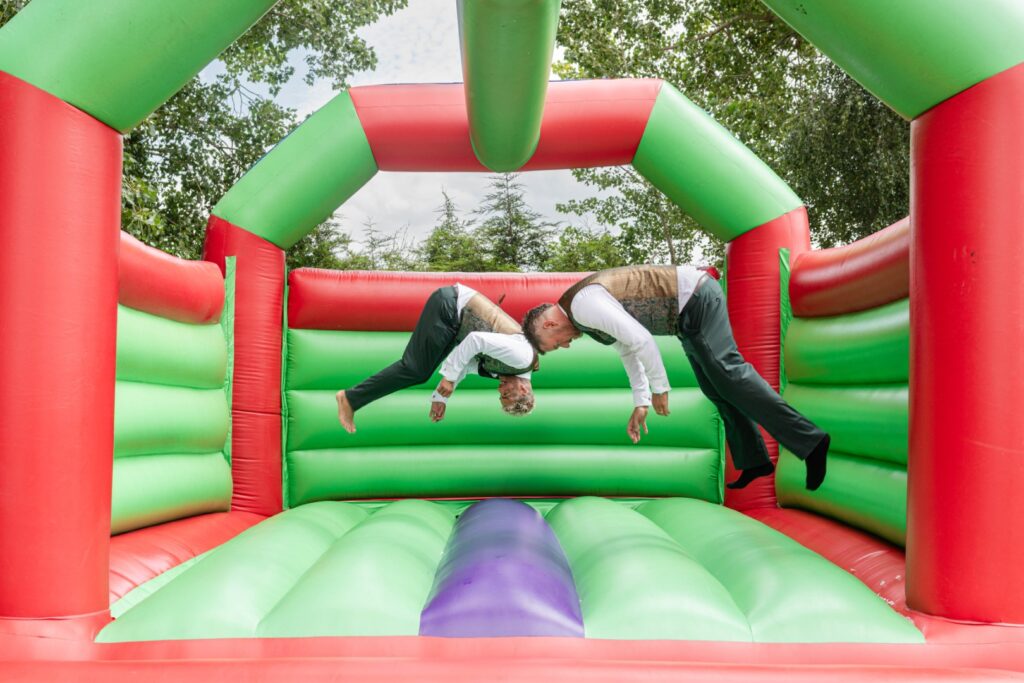 Grooms jumping on a colourful bouncy castle during their wedding – fun and natural moment captured by LB Photography